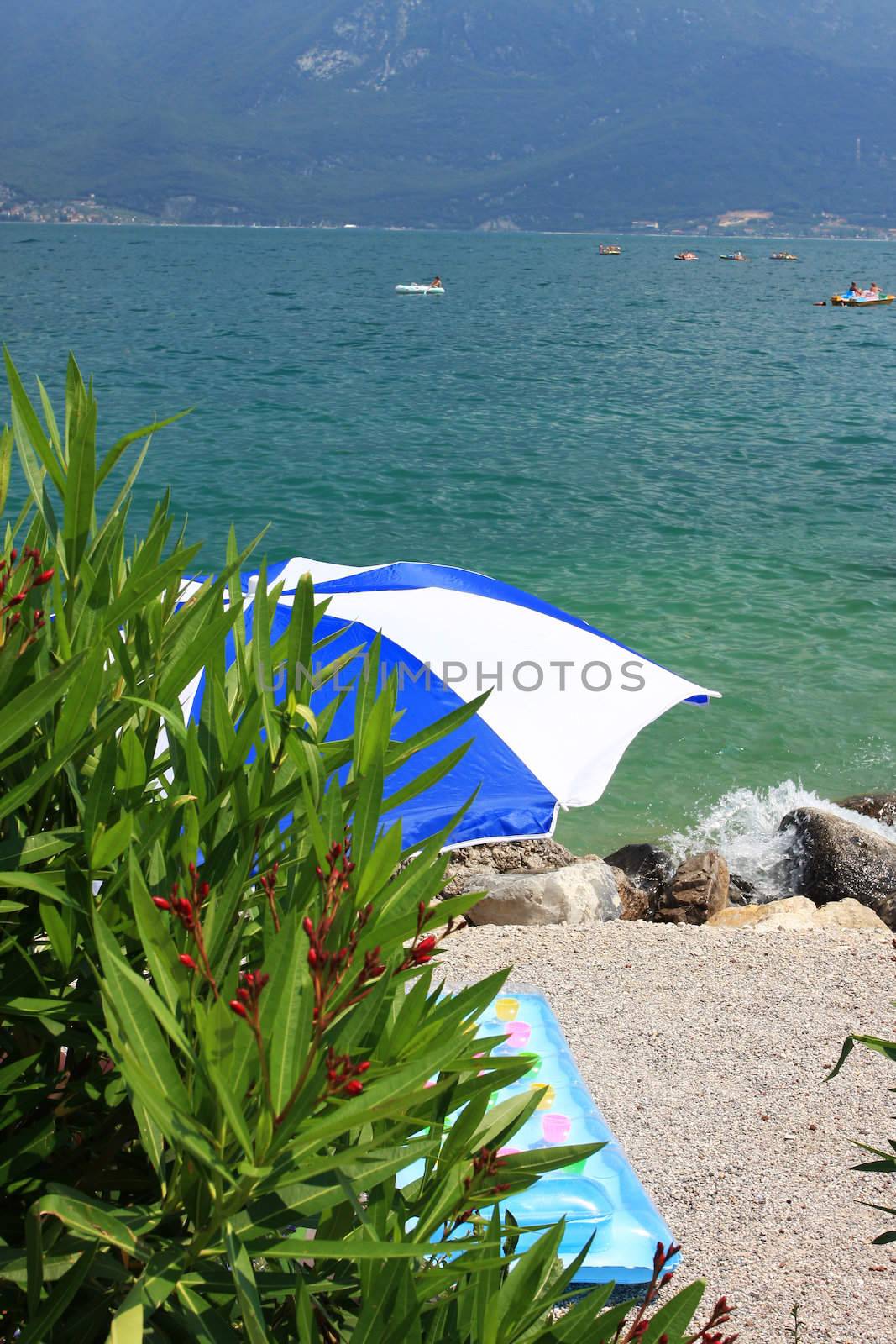 A beach umbrella on a beach at lake garda, colorful inflateable matress on the sand, fantastic holiday or vacation image,