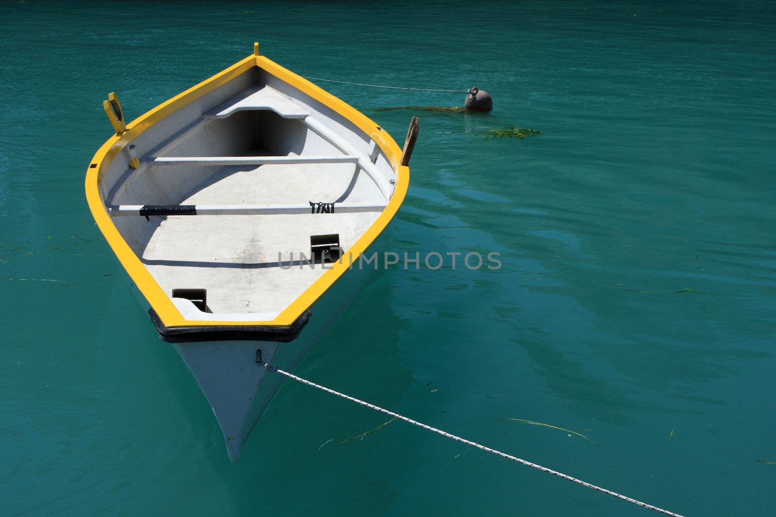 A yellow and white rowing boat on deep green water, plenty of copy space