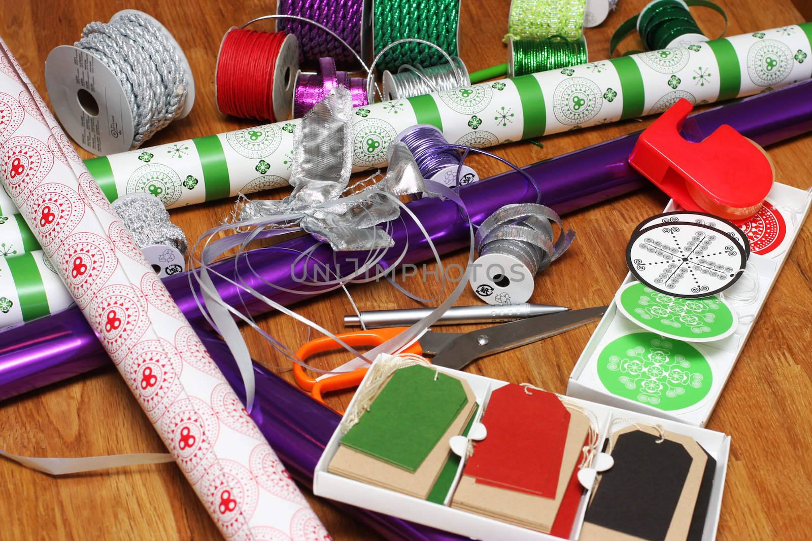 a bunch of wrapping paper, ribbons, label tags and other present wrapping material on an oak table