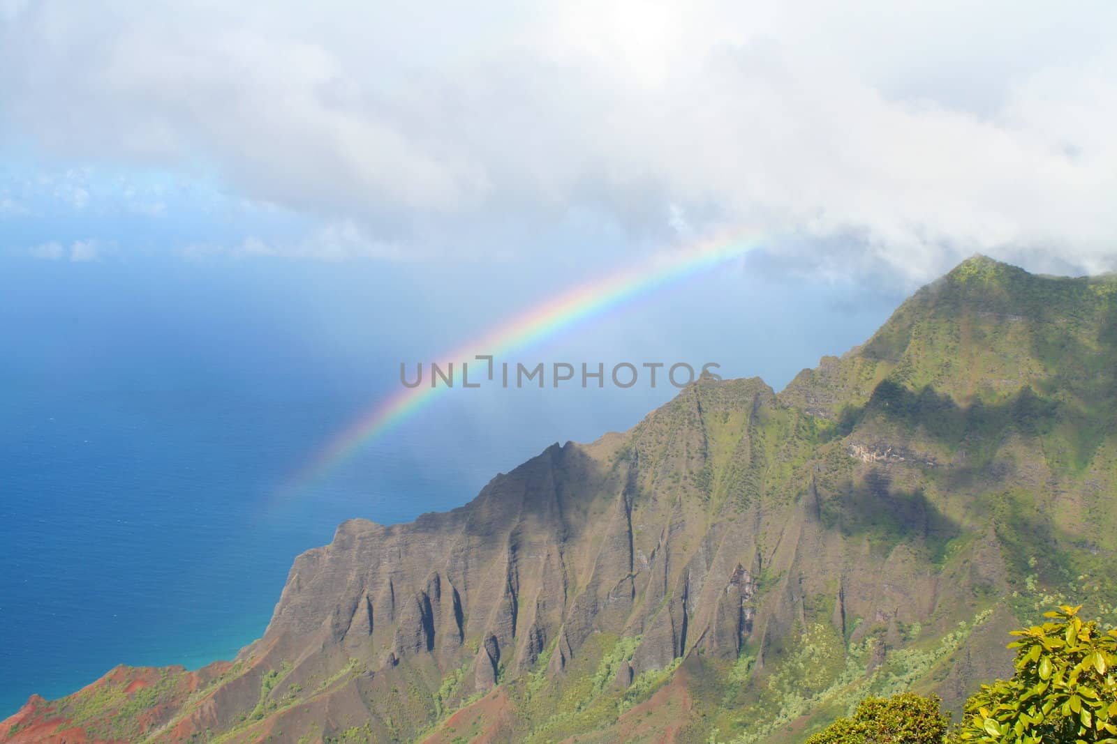 A rainbow stretches from the clouds to the sea.