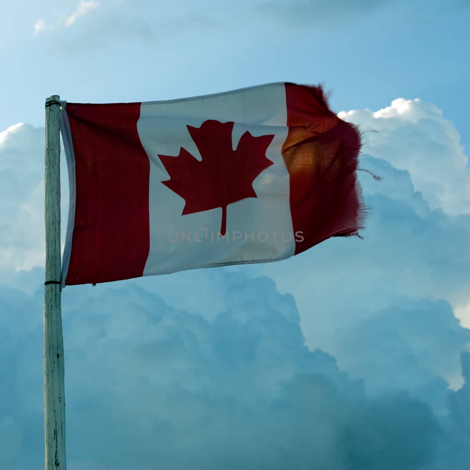 A traditional Canadian flag blowing in the wind, shot against some clouds