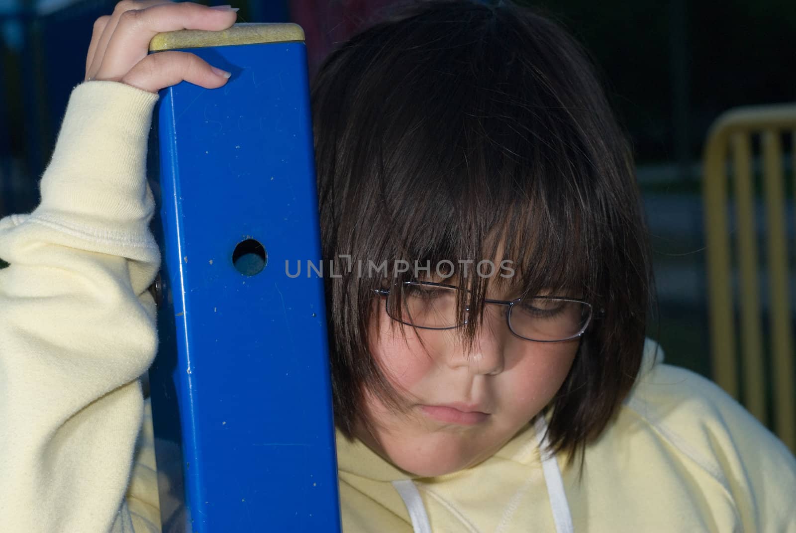 A young girl looking sad and depressed holding onto a blue pole