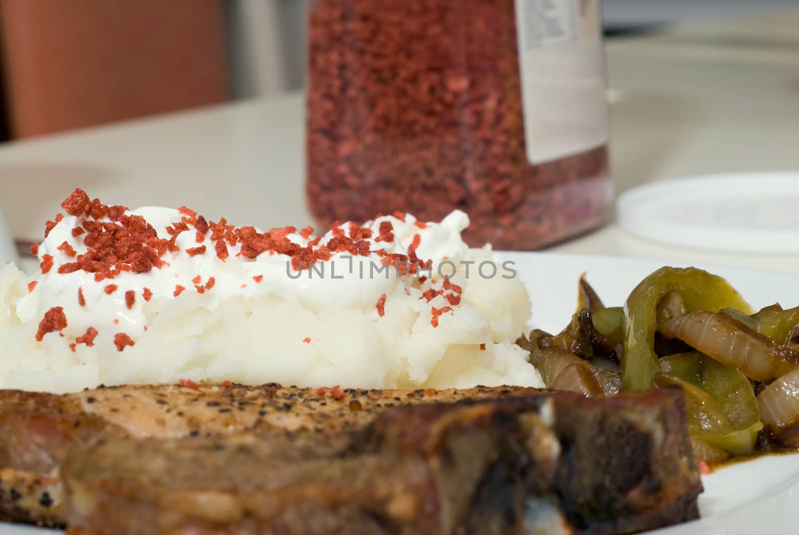 A plate of potatoes with sour cream and bacon bits, along with a pork chop and fried onions