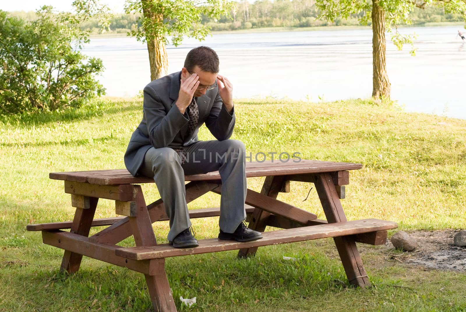 A young business worker sitting on a picnic table massaging his temples