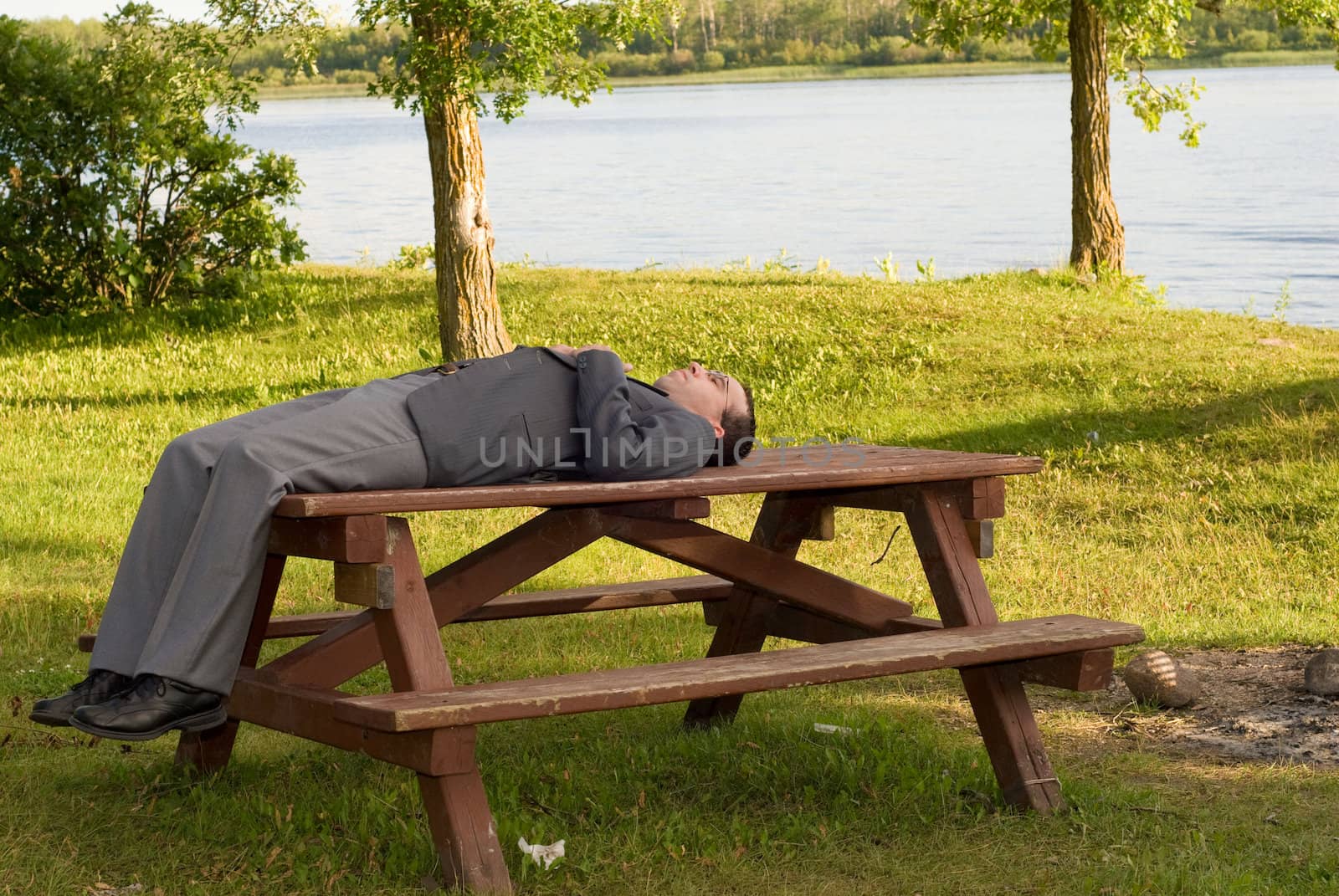 A young businessman lying on a table outside in a park