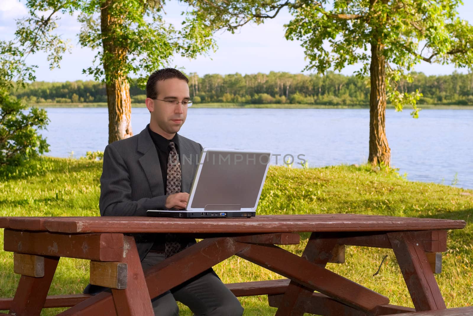 A young caucasian businessman working on a laptop computer outside in a park