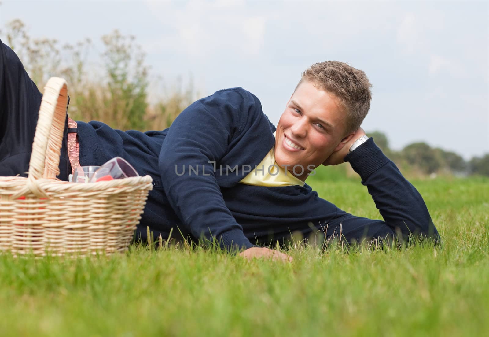 Young handsome blond lying on the grass with picnic basket