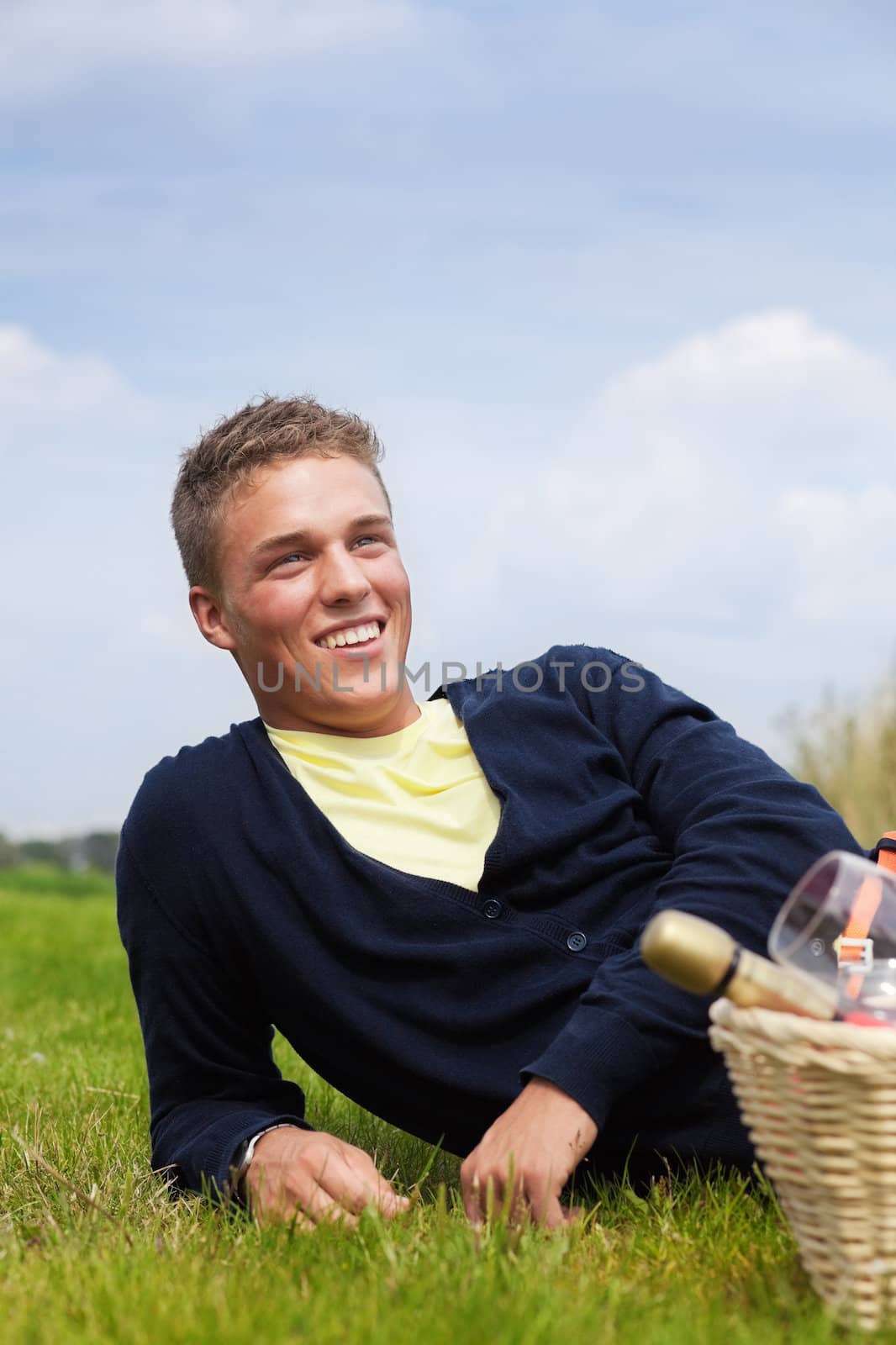 Young smiling man lying on the grass with picnic basket near him