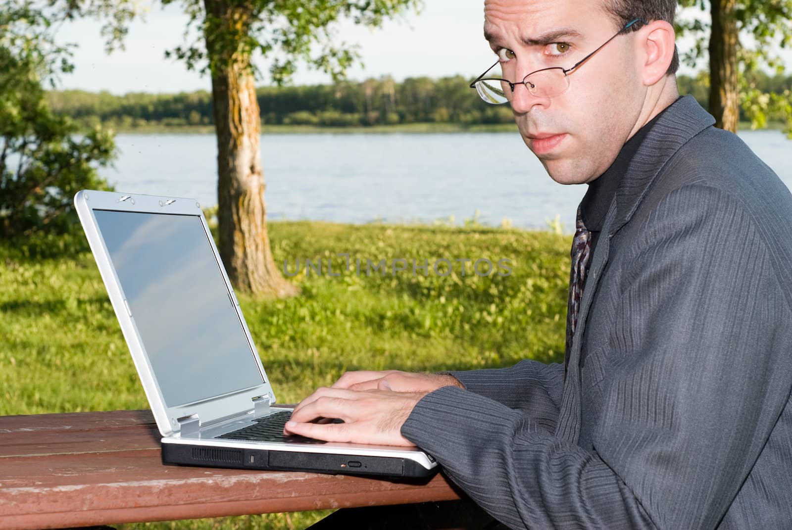 A serious employee working on his laptop outside in a park