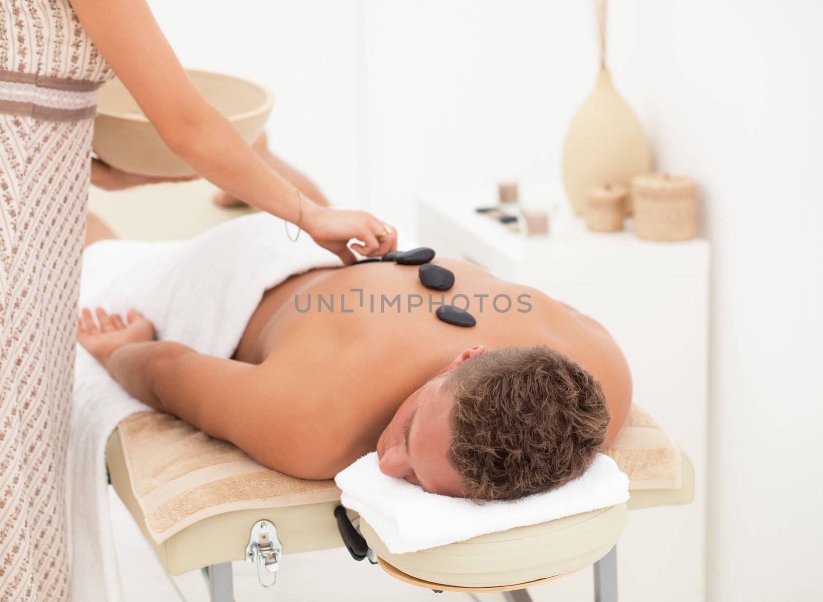 Therapist putting stones on the back of young blond man