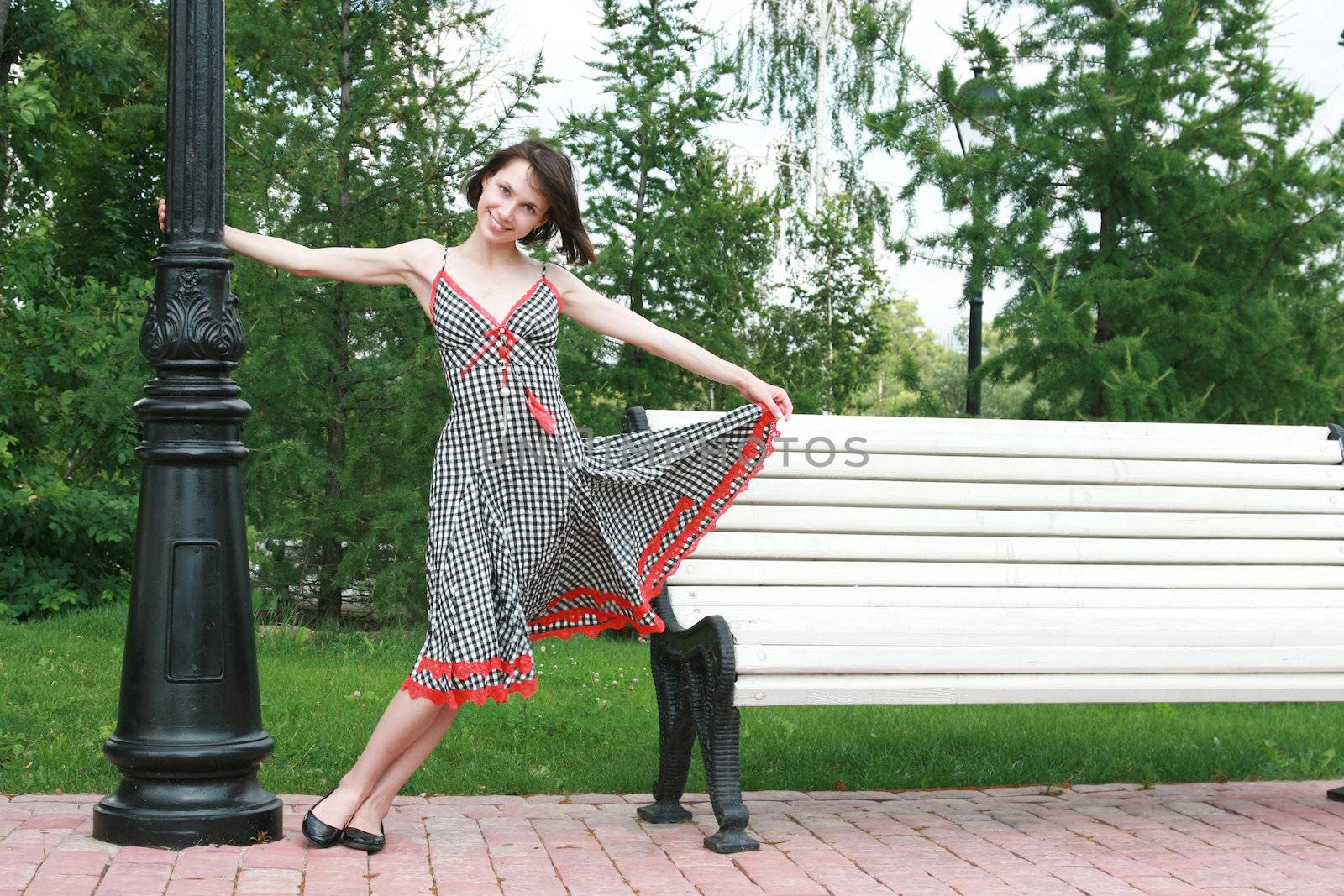 The beautiful girl poses at a lamppost and a bench
