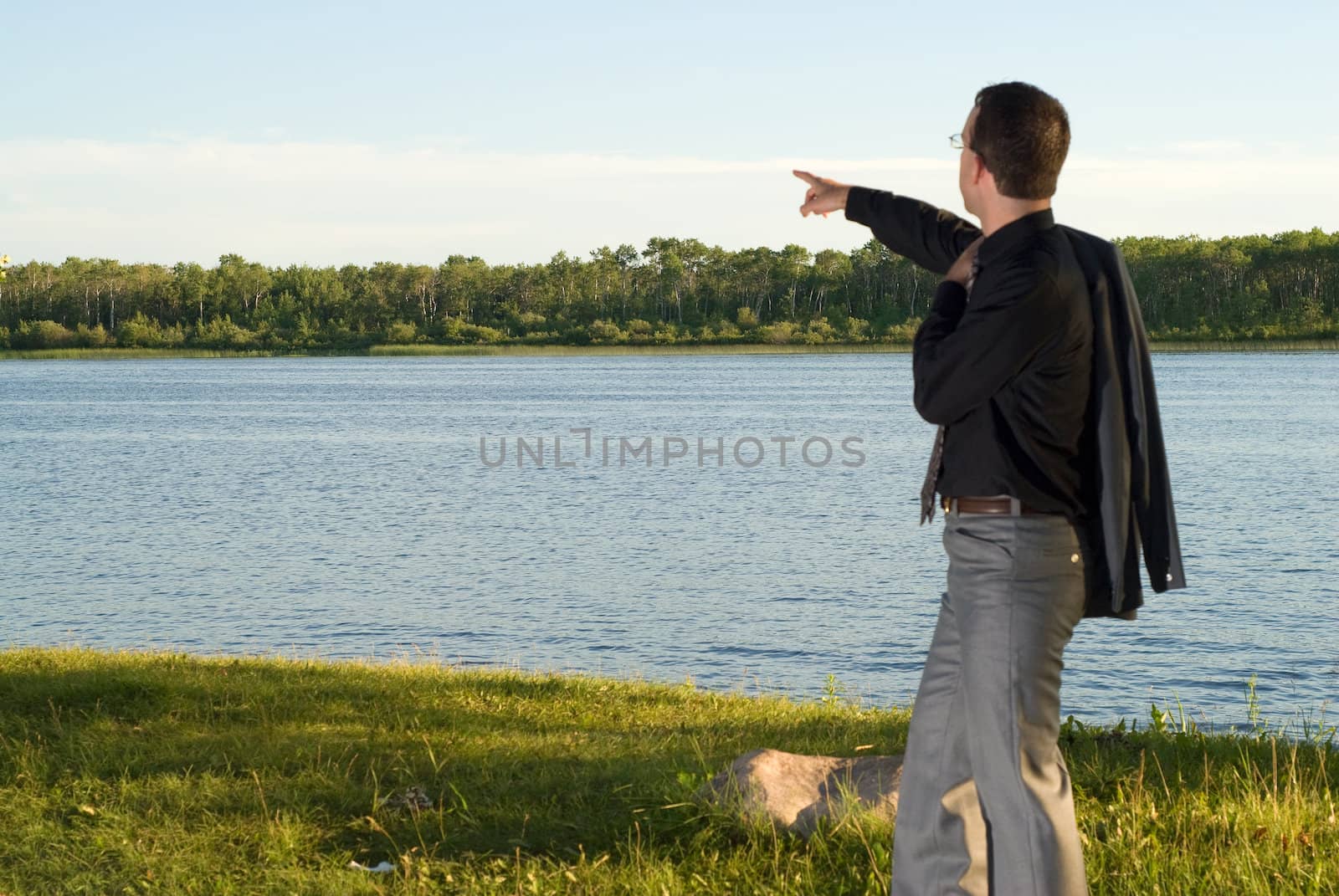 A young businessman out of focus, pointing at something over the lake