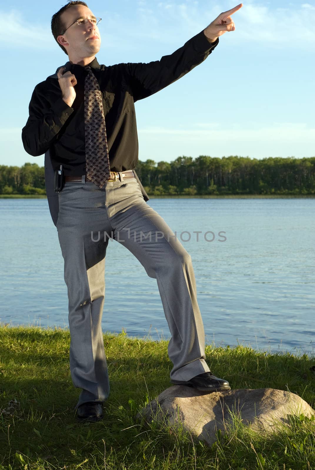 A young businessman posing on a rock and pointing at something