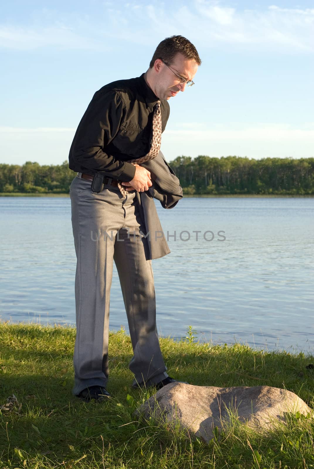 A young businessman holding his stomach at the lake, because he has a stomach ache