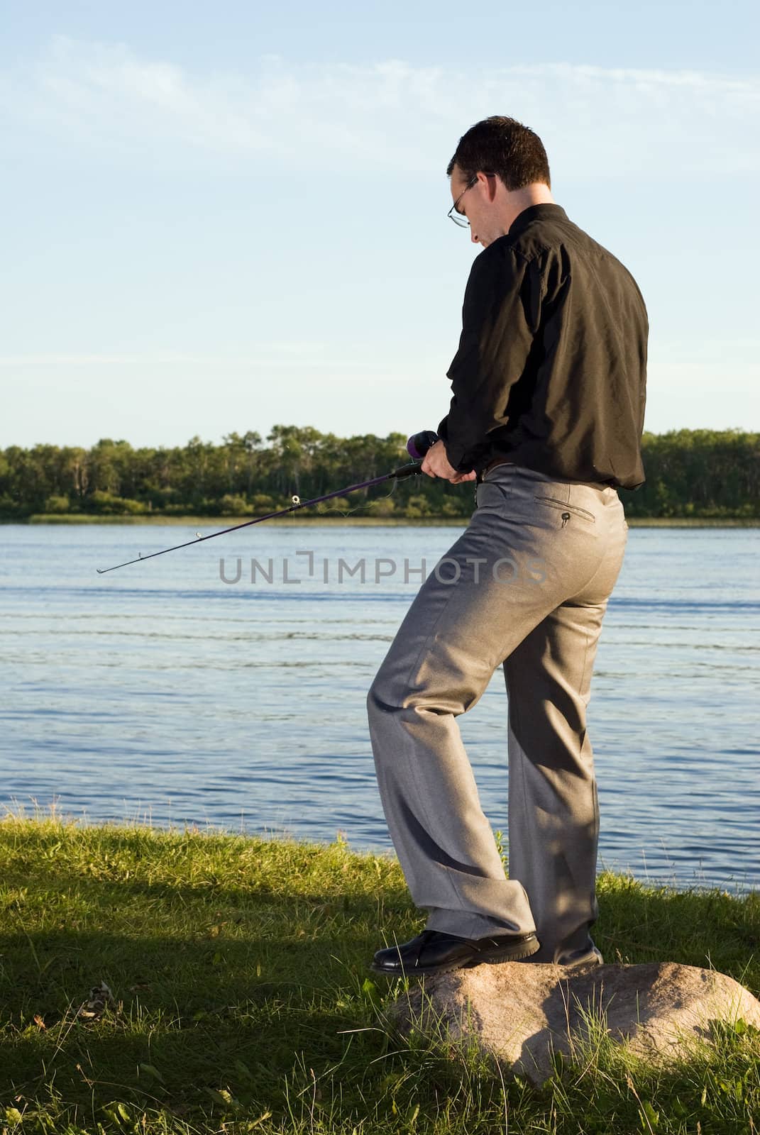 A young man wearing a suit, going fishing in a small lake