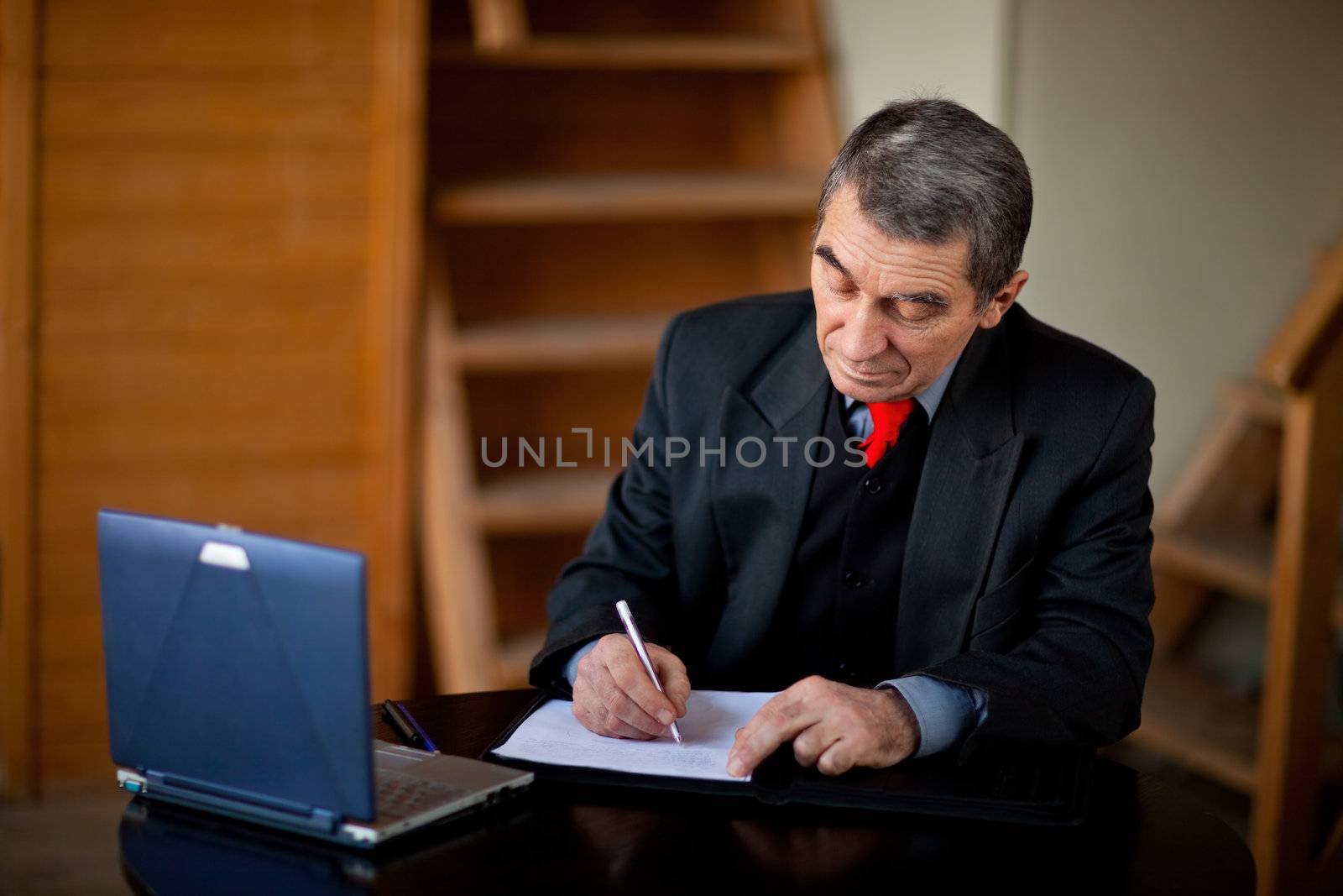 Senior businessman writing and working with document indoors