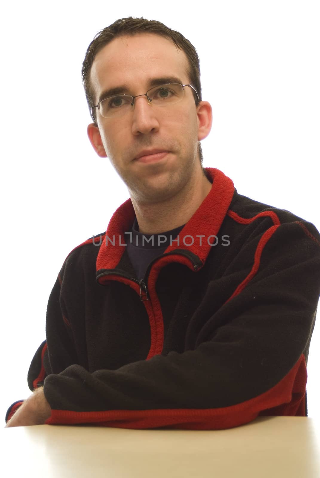 A young man wearing a black sweat shirt with red trim, leaning on a table.