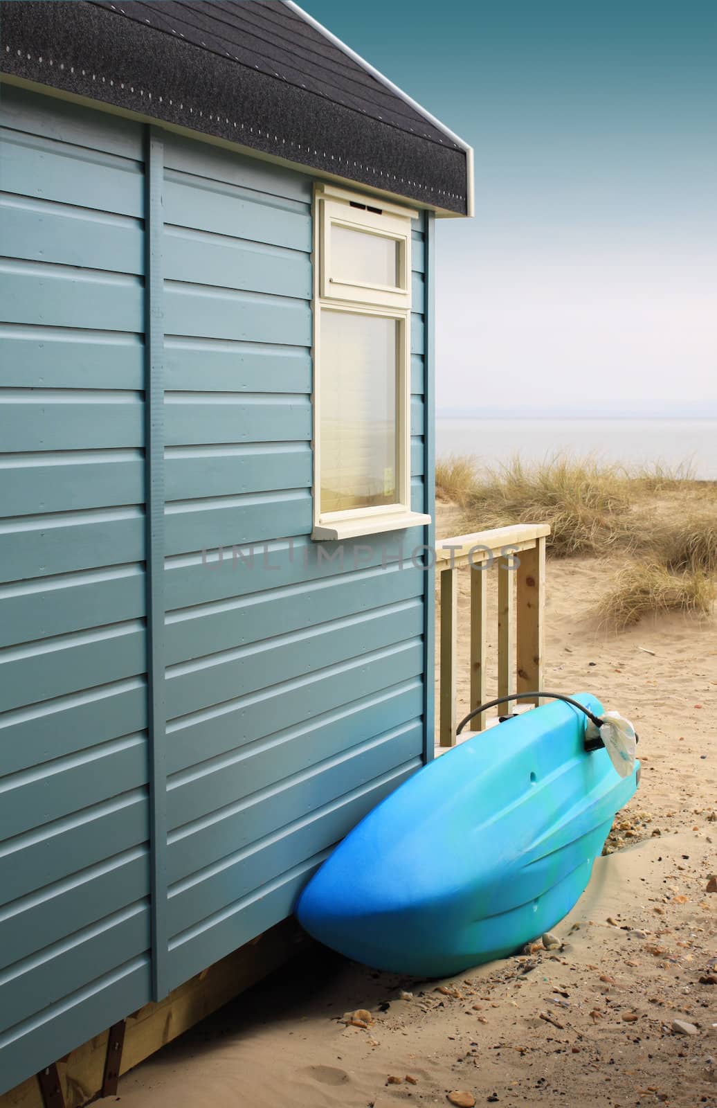 View of the side of a wooden beach hut with a blue surf board, looking towards the beach. Located in Christchurch, Dorset Hampshire UK.