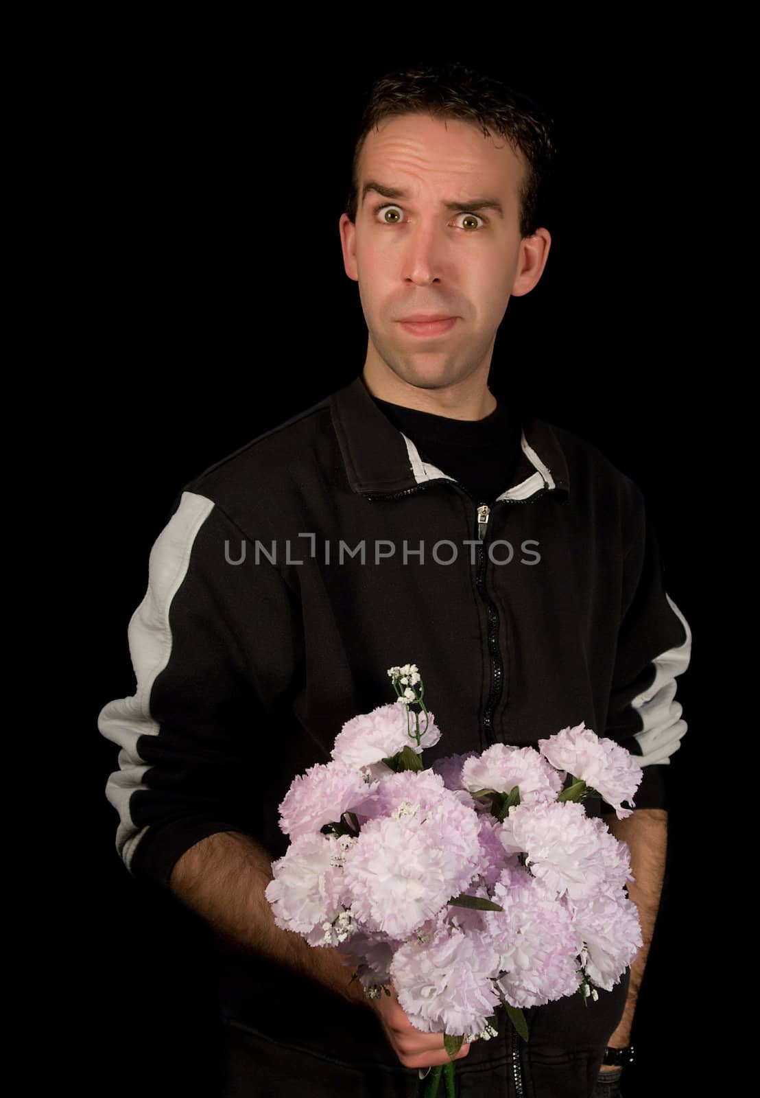 Young man holding a bouquet of flowers with a funny expression on his face, isolated against a black background