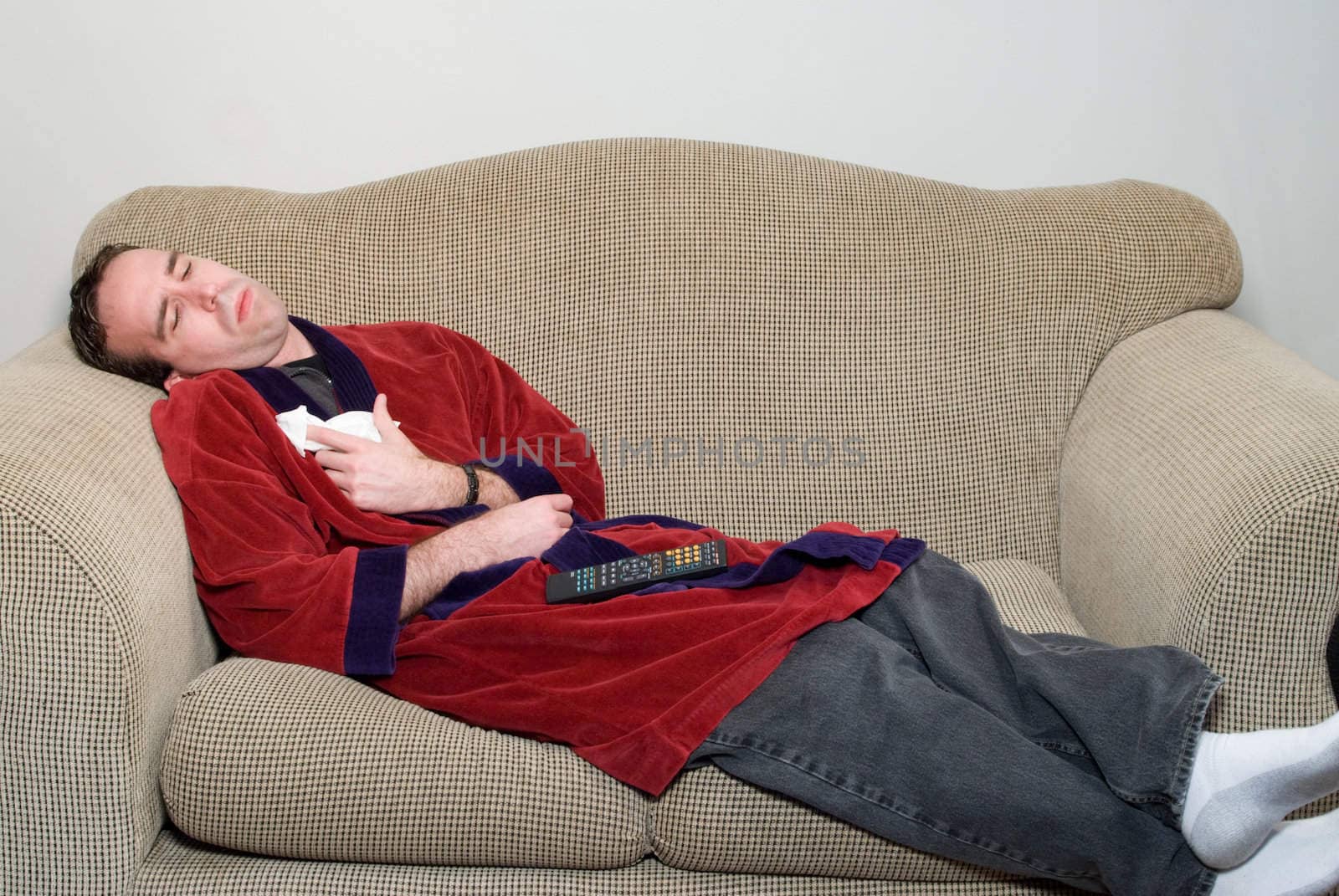 A young man laying on a sofa in his bathrobe, feeling ill because he has the flu