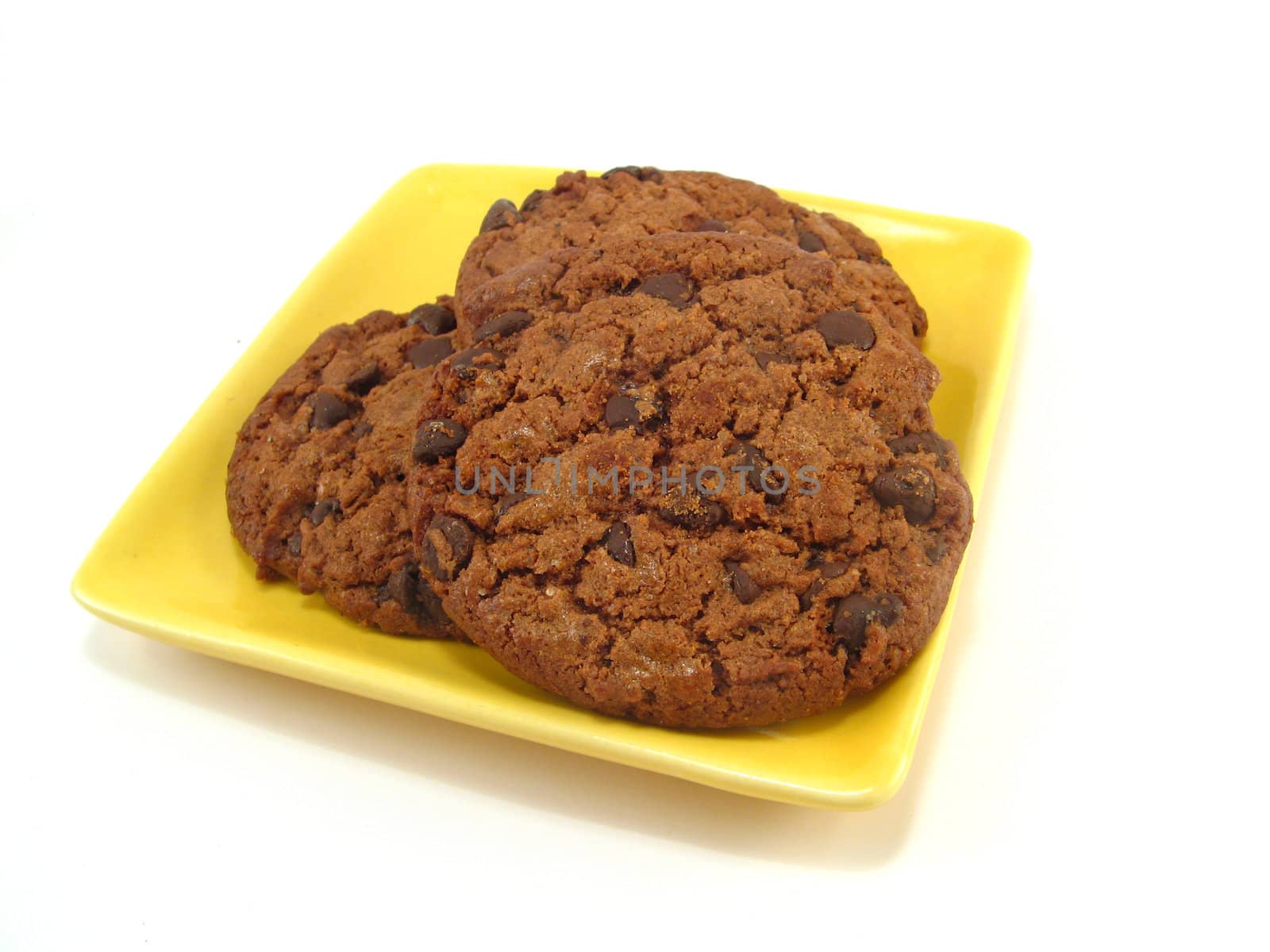 some chocolate cookies on a yellow plate over a white background