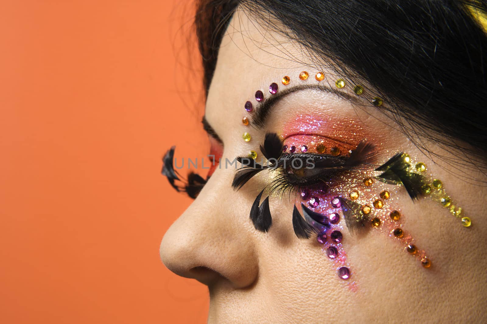 Close-up of Caucasian woman in unique makeup against orange background.