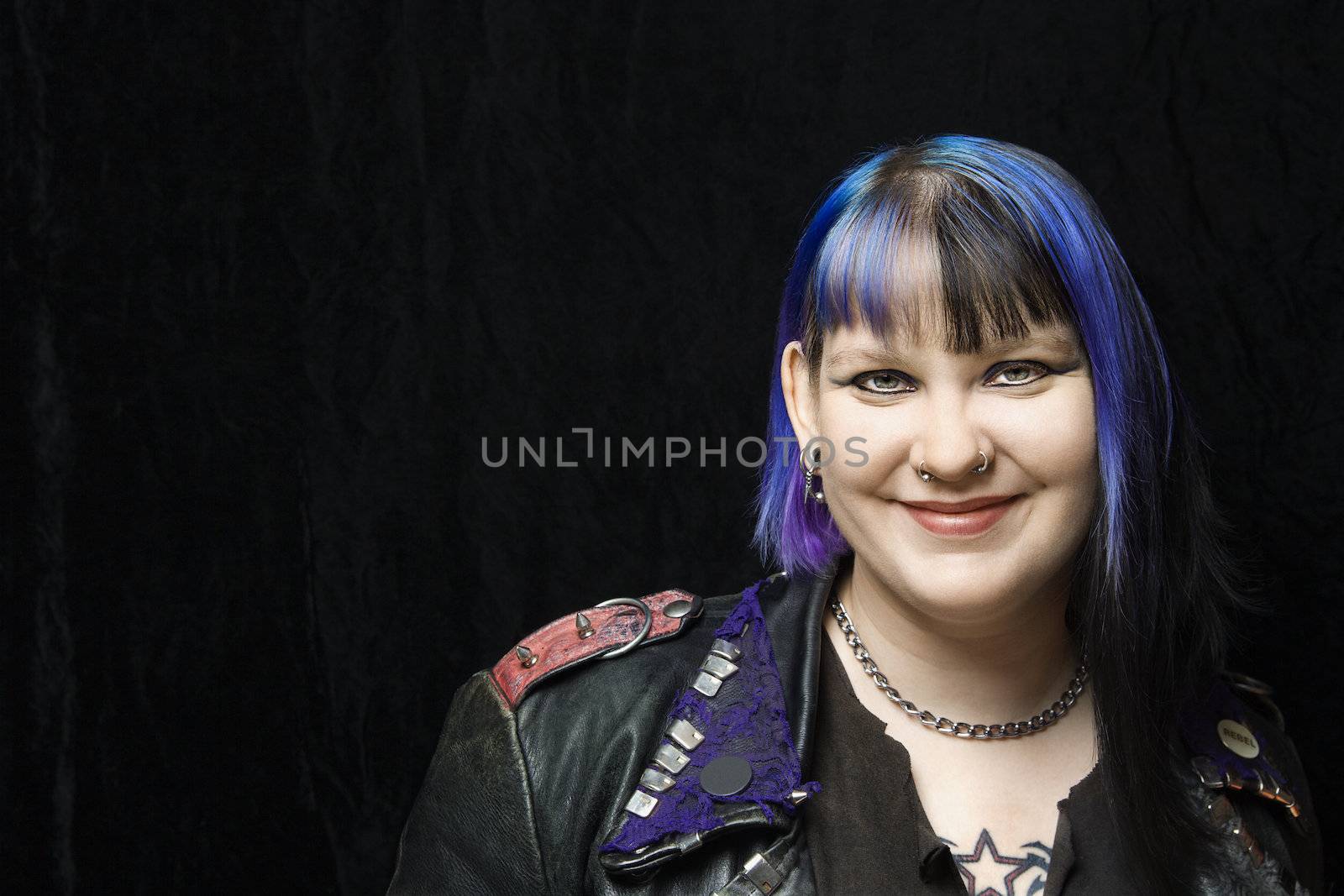 Portrait of smiling Caucasian woman with blue hair and black leather jacket against black background.