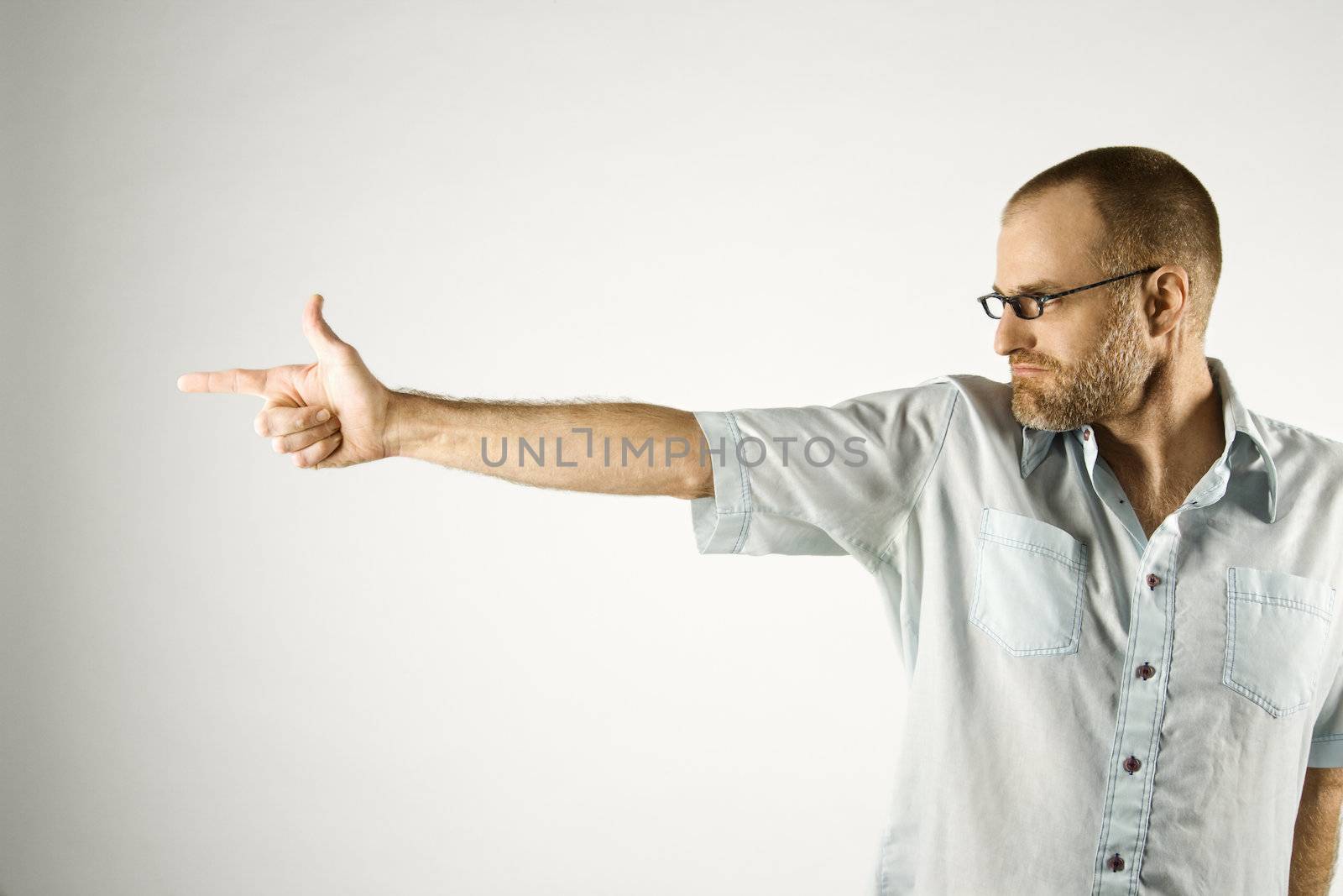 Portrait of Caucasian man holding hand out like a gun standing against white background.