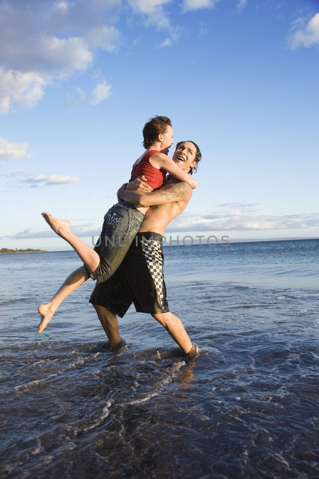 Caucasian young adult couple frolicking on beach.