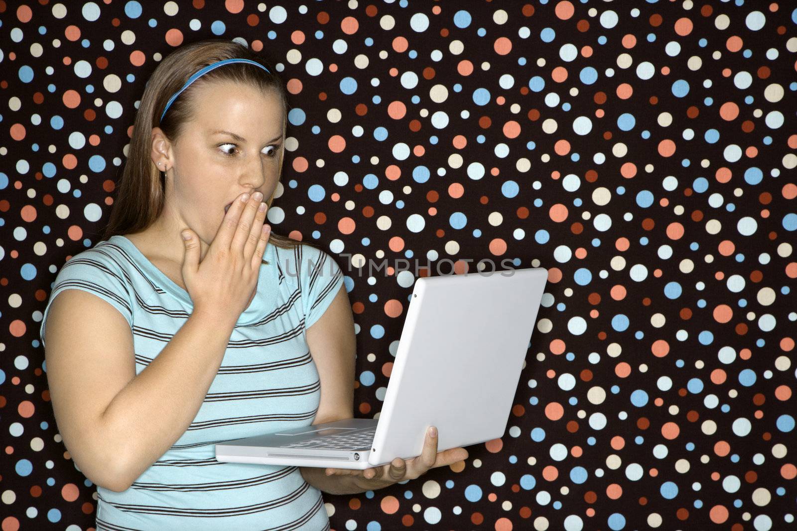 Young Caucasian woman holding laptop looking shocked.