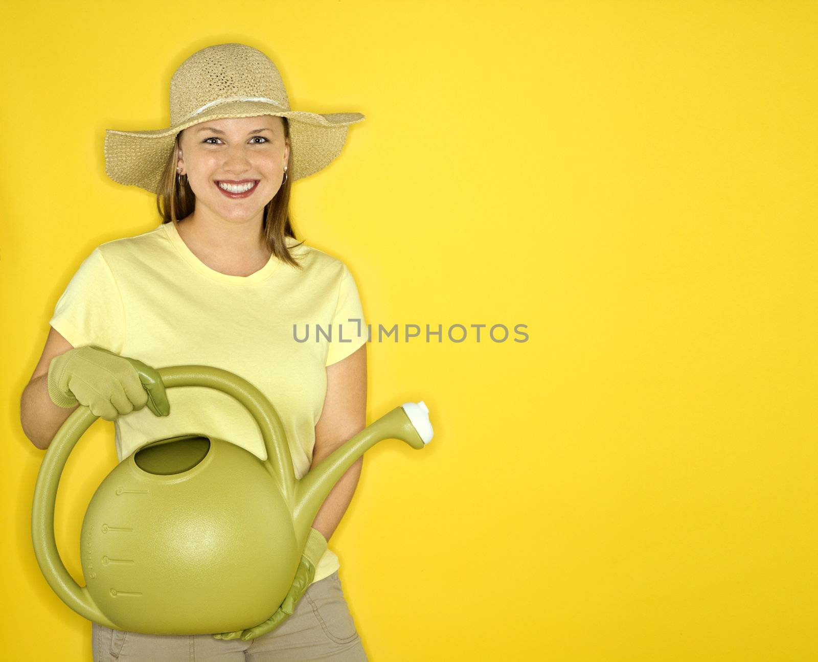 Young adult female Caucasian holding watering can wearing straw hat.