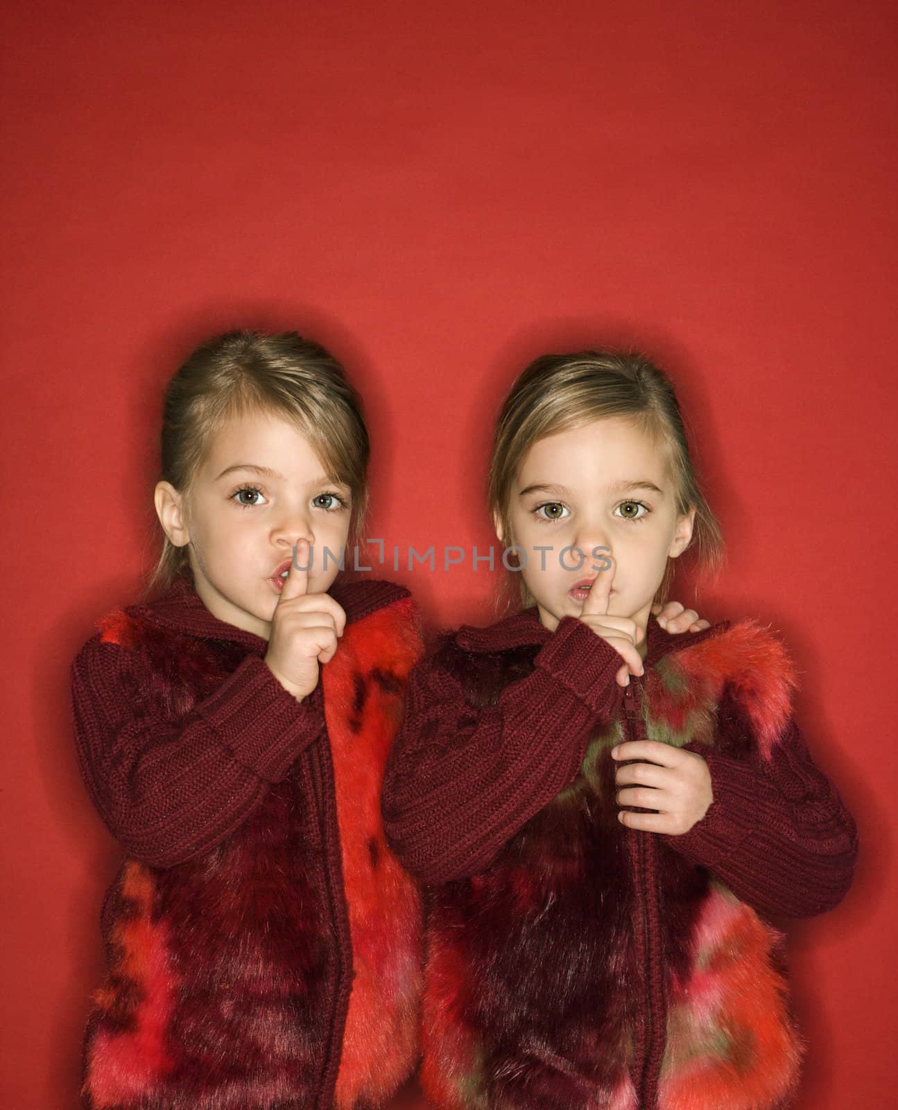 Female children Caucasian twins with fingers up to lips.