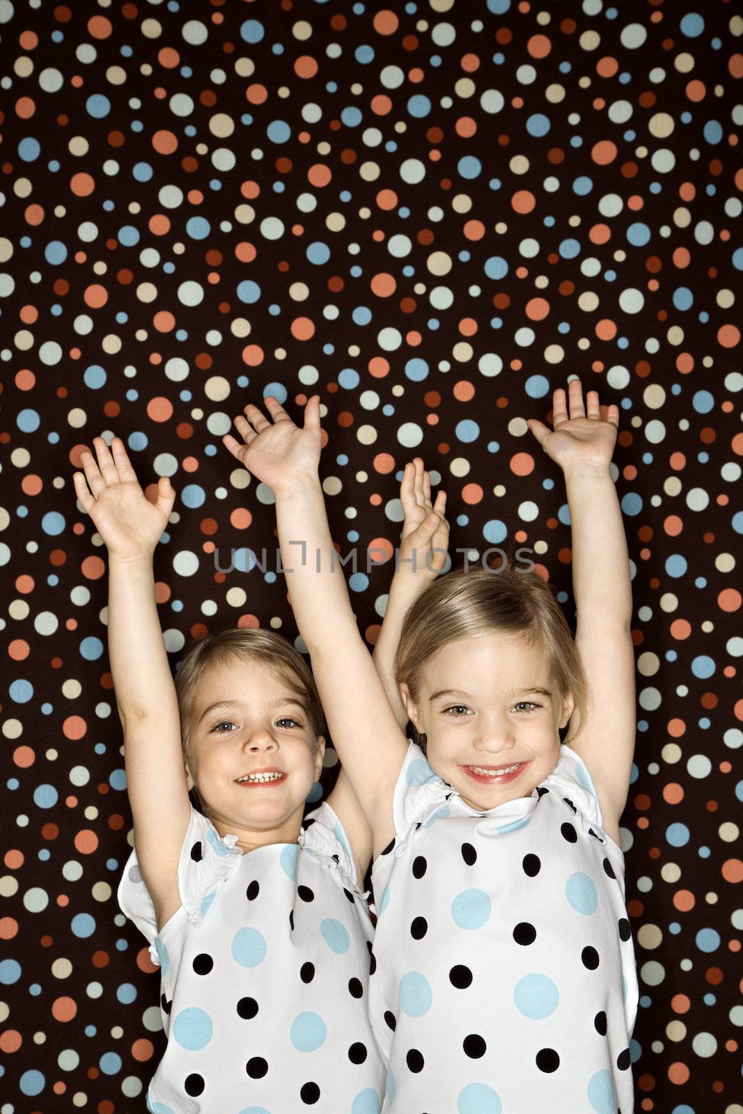 Female children Caucasian twins looking at viewer with arms raised.
