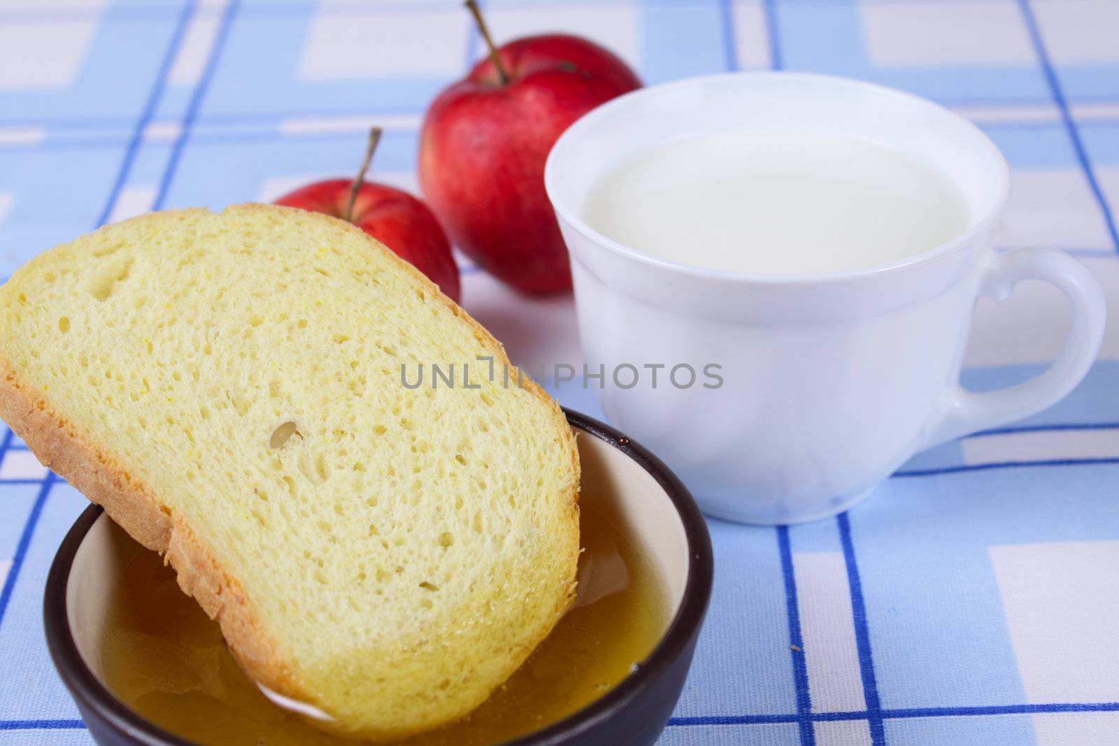 Cup of milk with a cornbread, honey and red apples removed close up