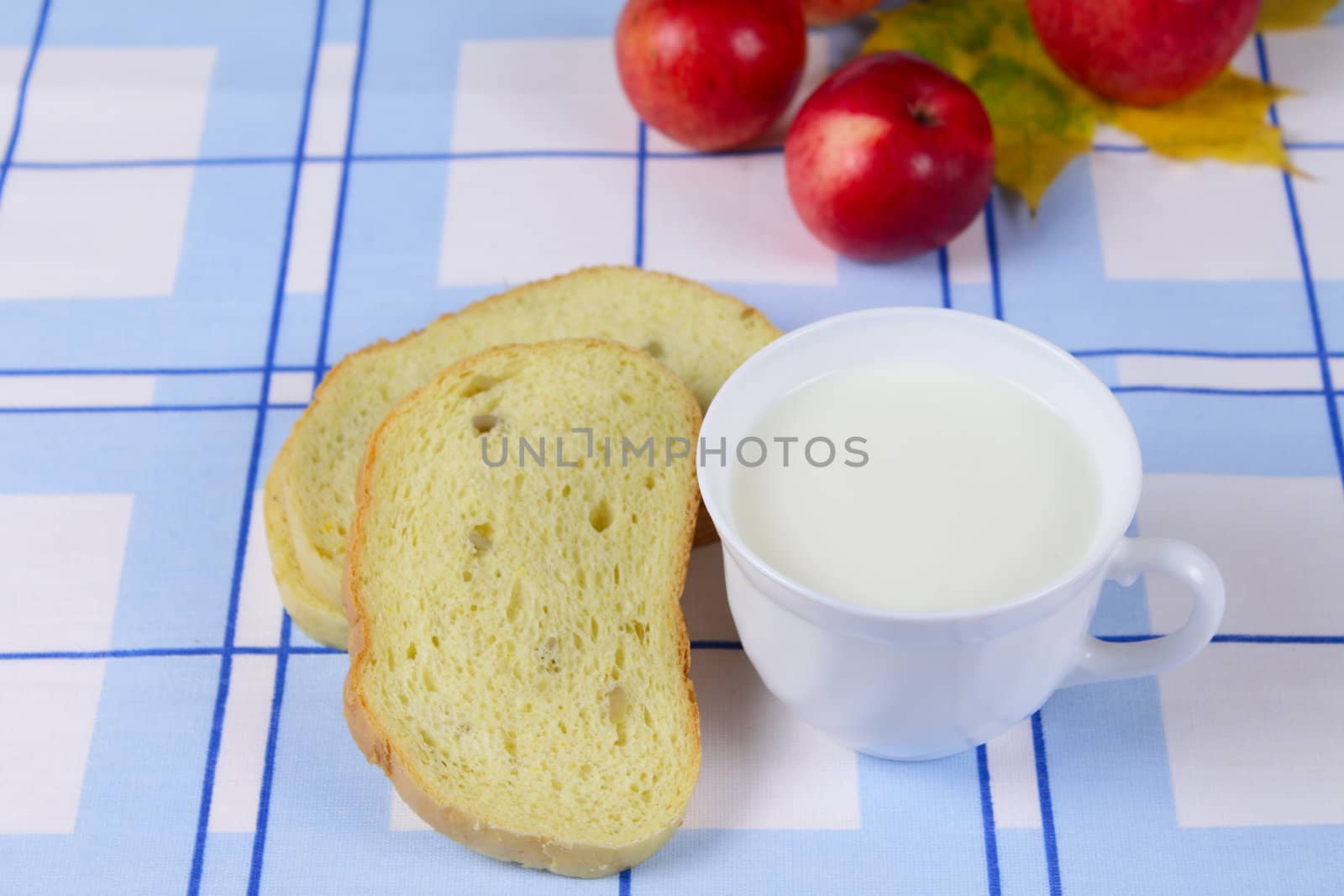 Cup of milk with a cornbread and apples on a blue linen napkin removed close up