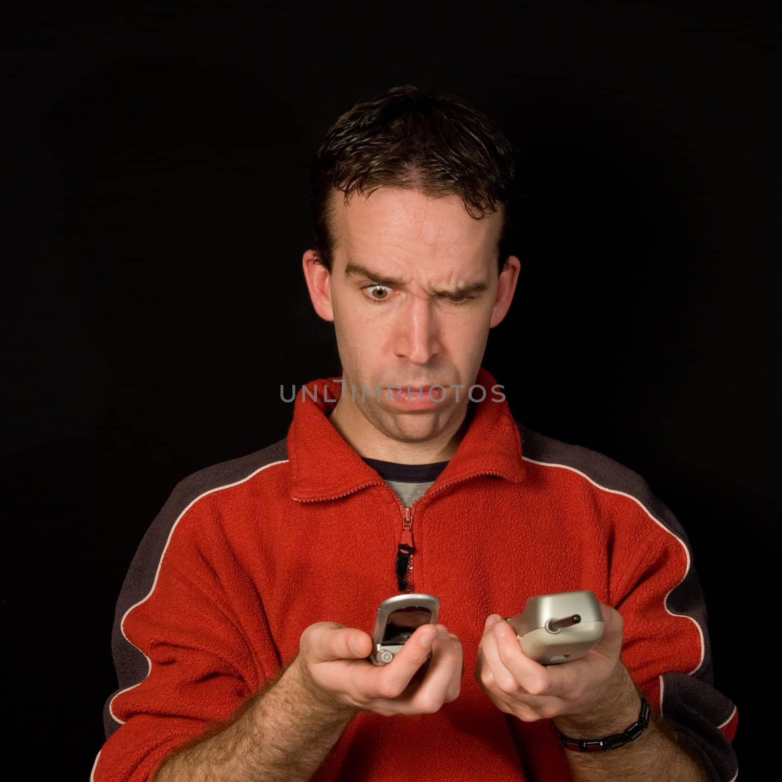 Young man comparing phones isolated against a dark background