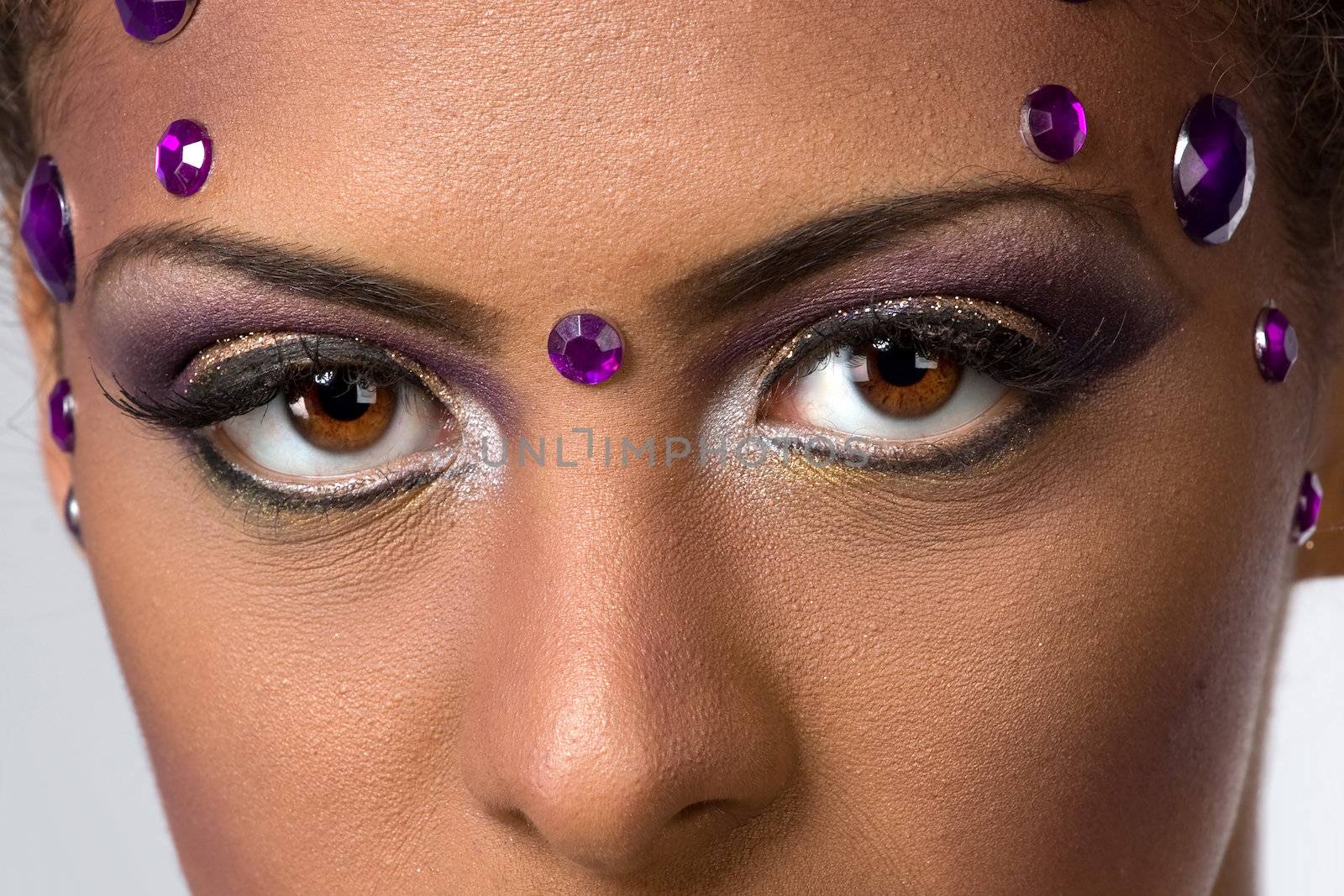 A closeup of a womans eyes with extravagant and glamorous makeup and gemstones looking very seductive.