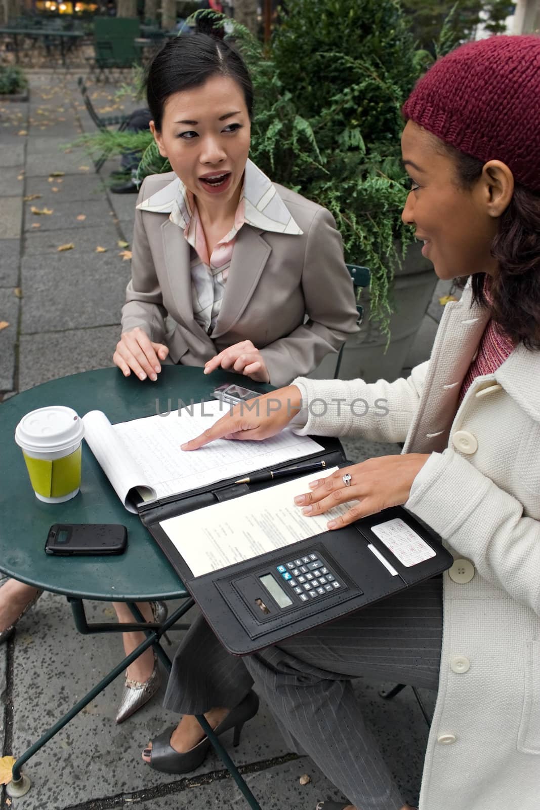 Two young business women discussing a group or team project in the park.