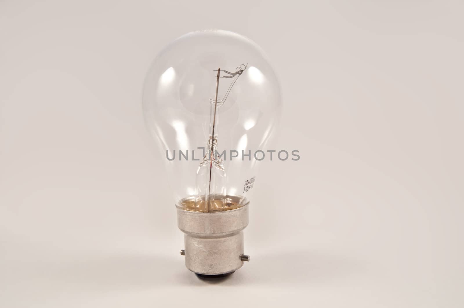 Close on an isolated clear glass light bulb arranged vertically over light grey.