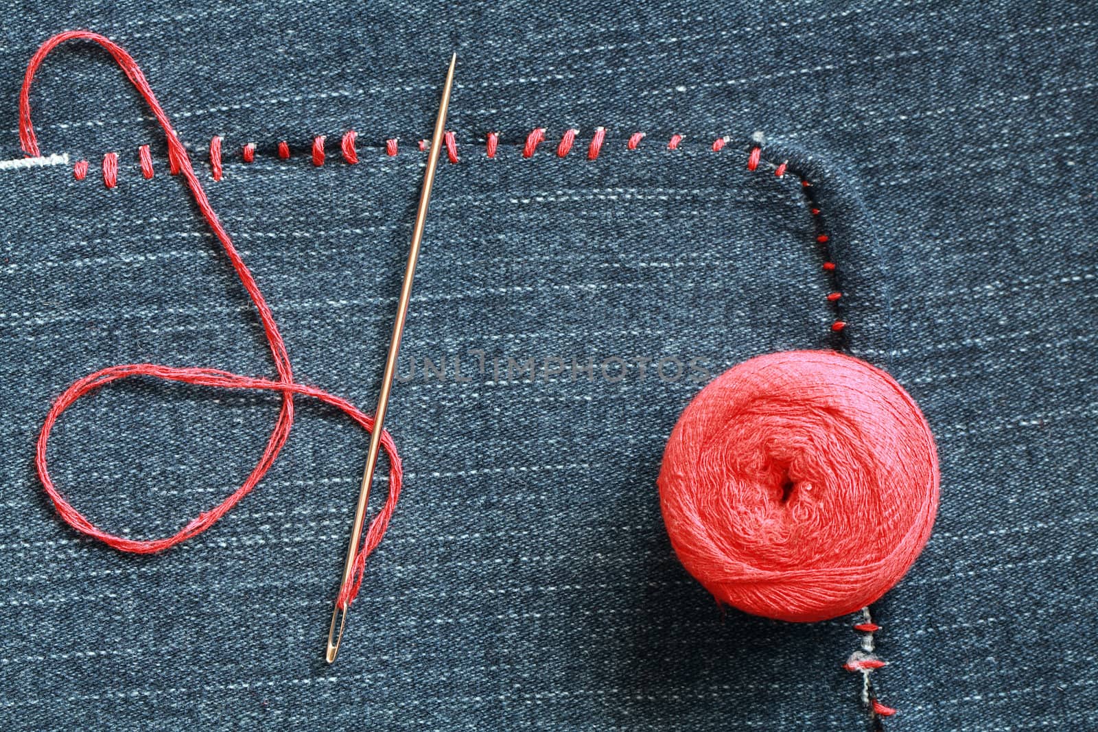 Closeup of needle and red thread on hole-ridden jeans textured