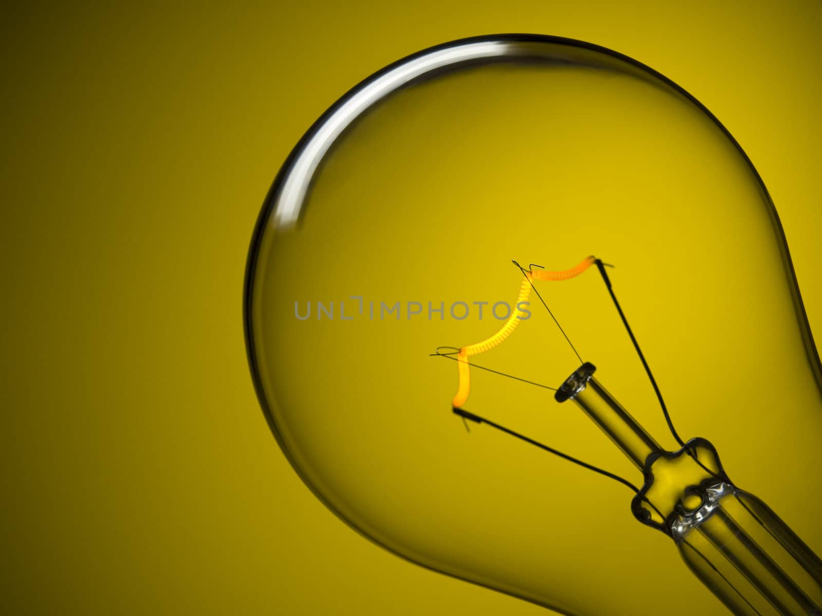 Close up on a turned on light bulb over a yellow background.