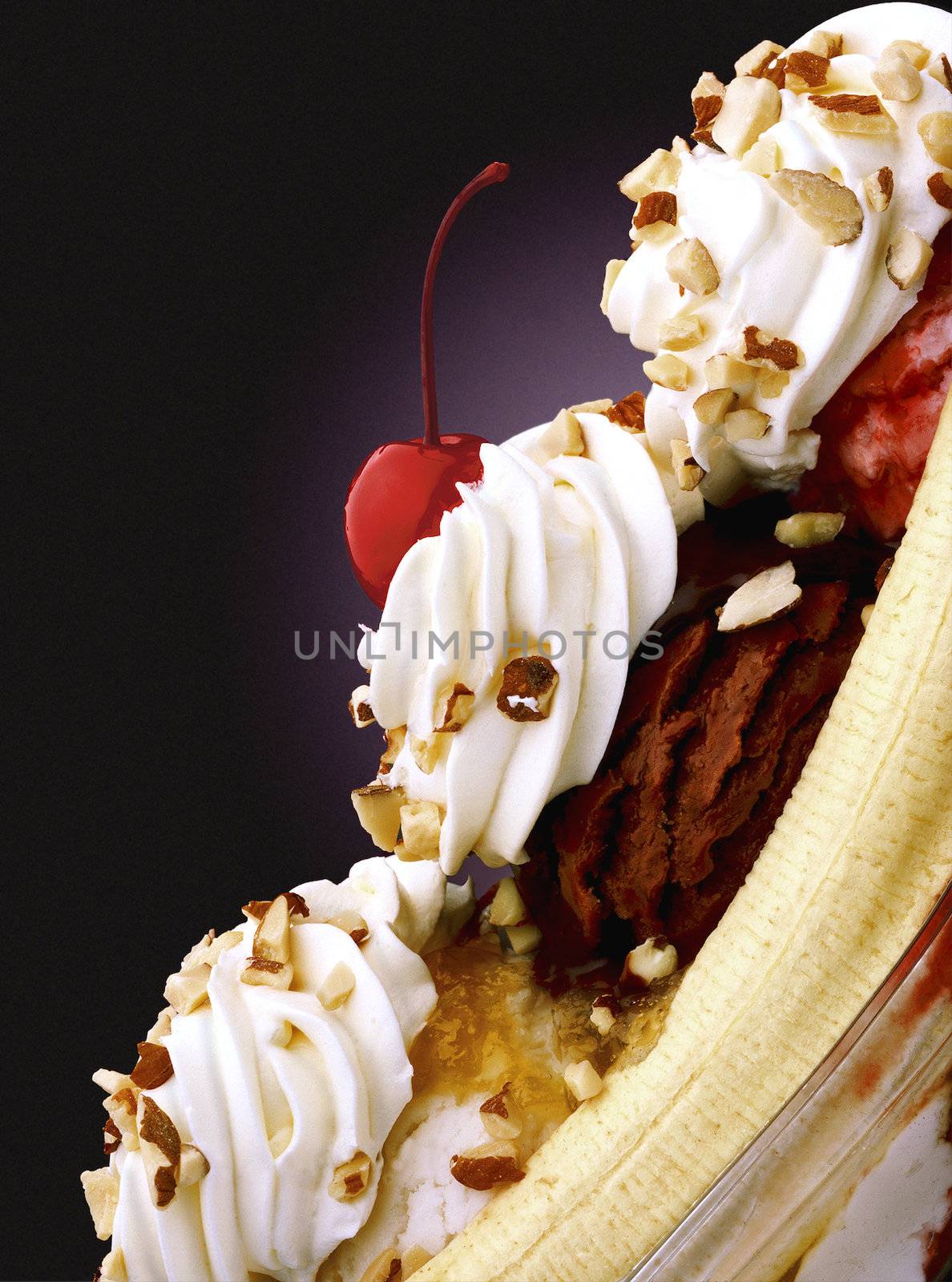 Vertical shot of a banana split with three kinds of syrup, whipped cream, nuts, with a cherry on top.