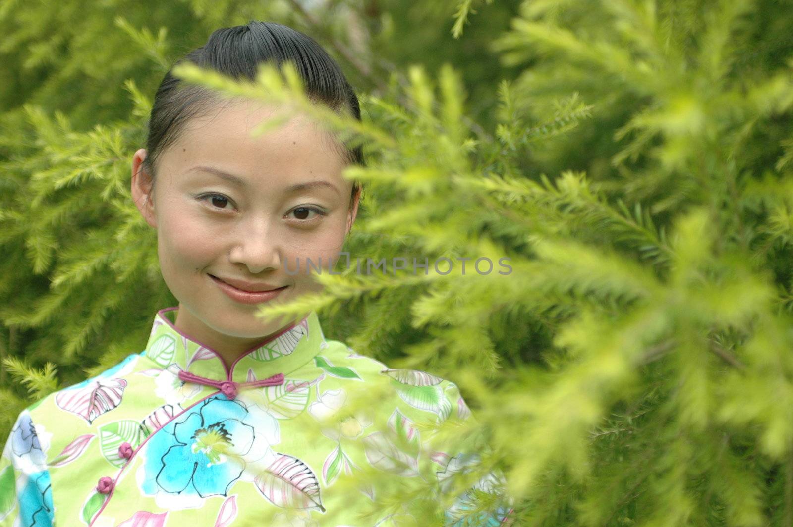 Chinese girl in park, hidding behind green bushes.