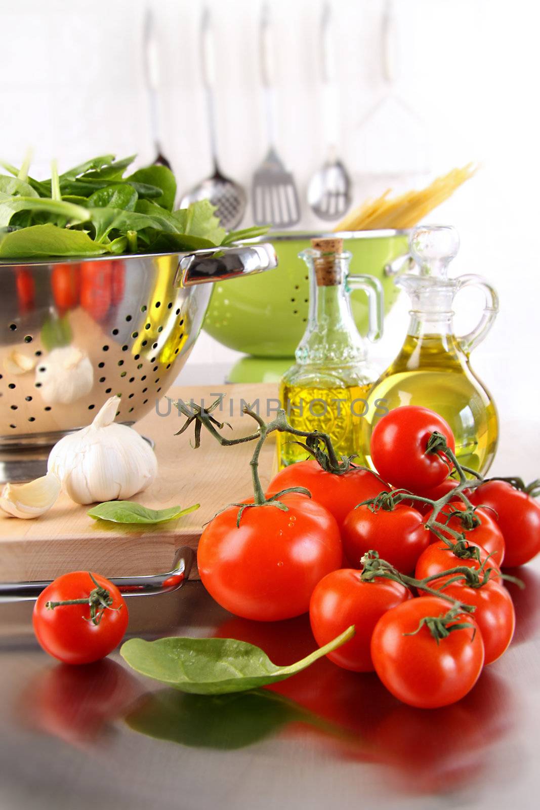 Spinach leaves in strainer with tomatoes on stainless steel counter