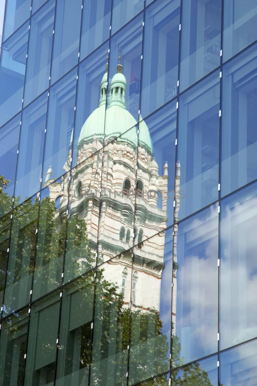 An old tower reflected in athe glass of a modern building