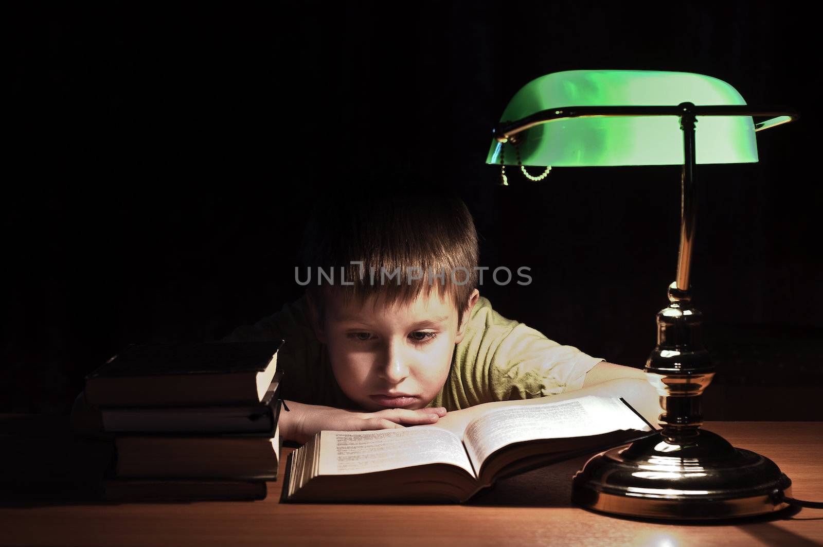 boy reads book in dark room under green lamp