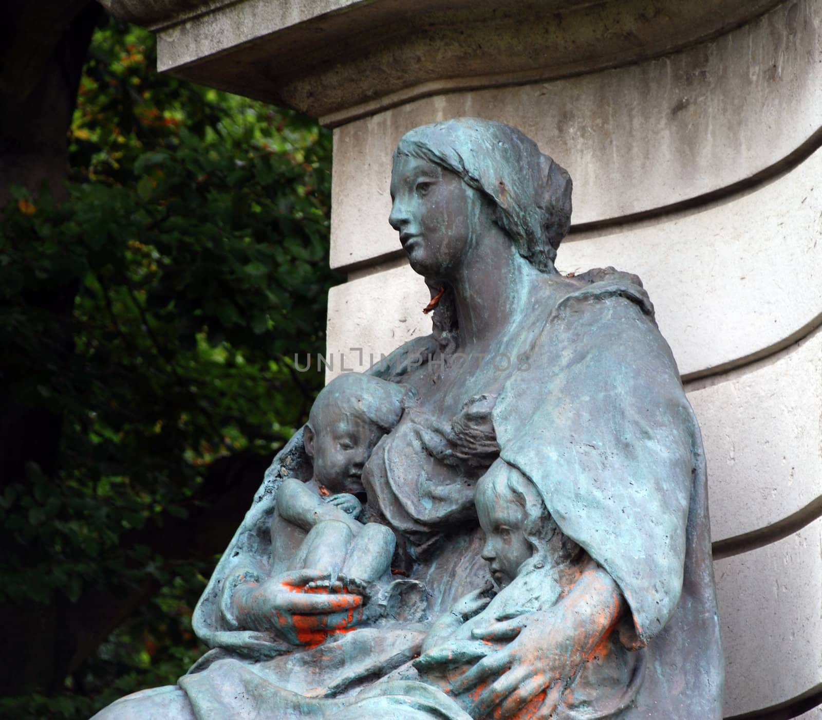 A statue of a woman holding two children which has turned blue green over time due to the nature of the metal