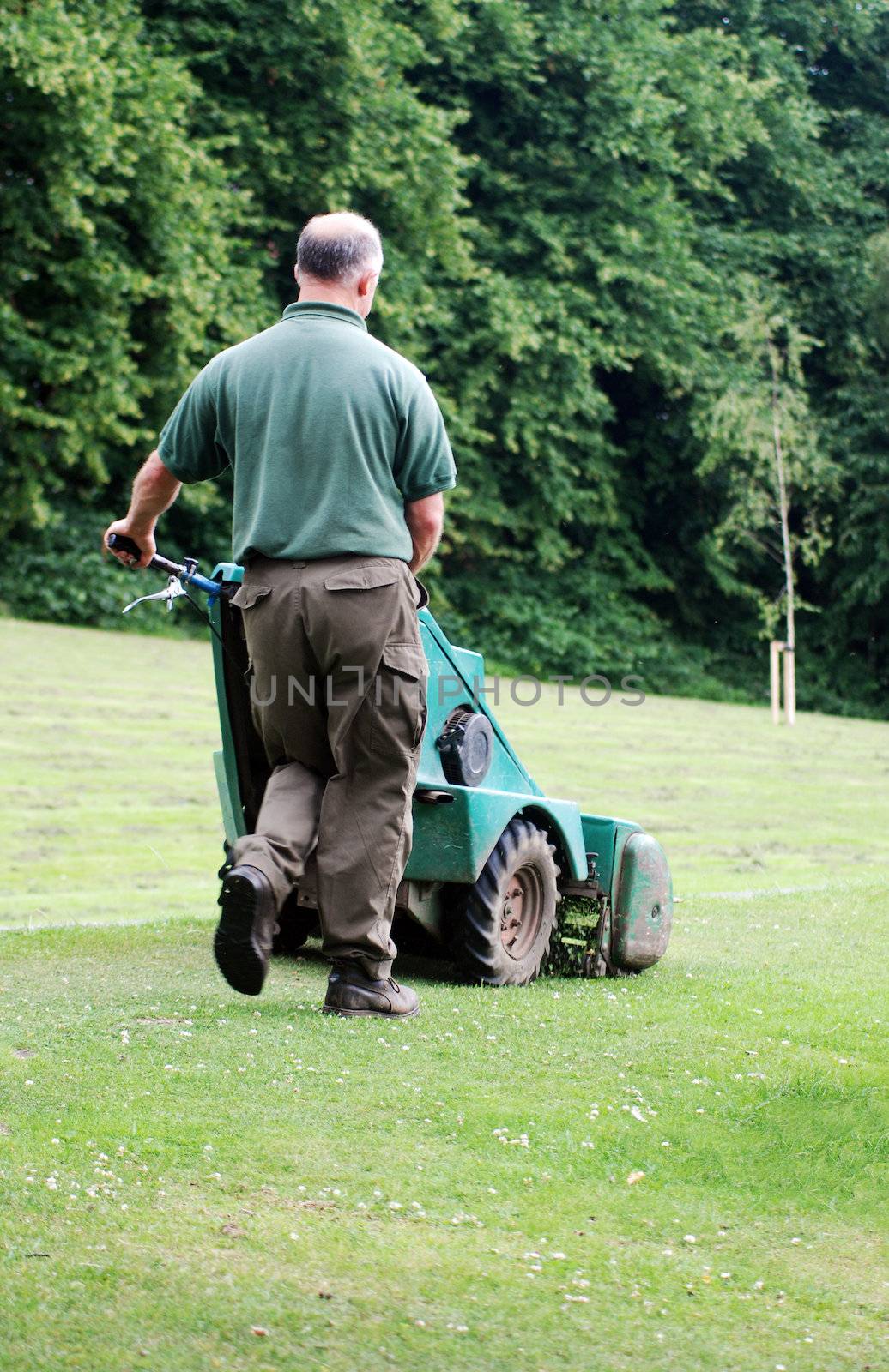 A photograph of a man mowing the grass in a public park