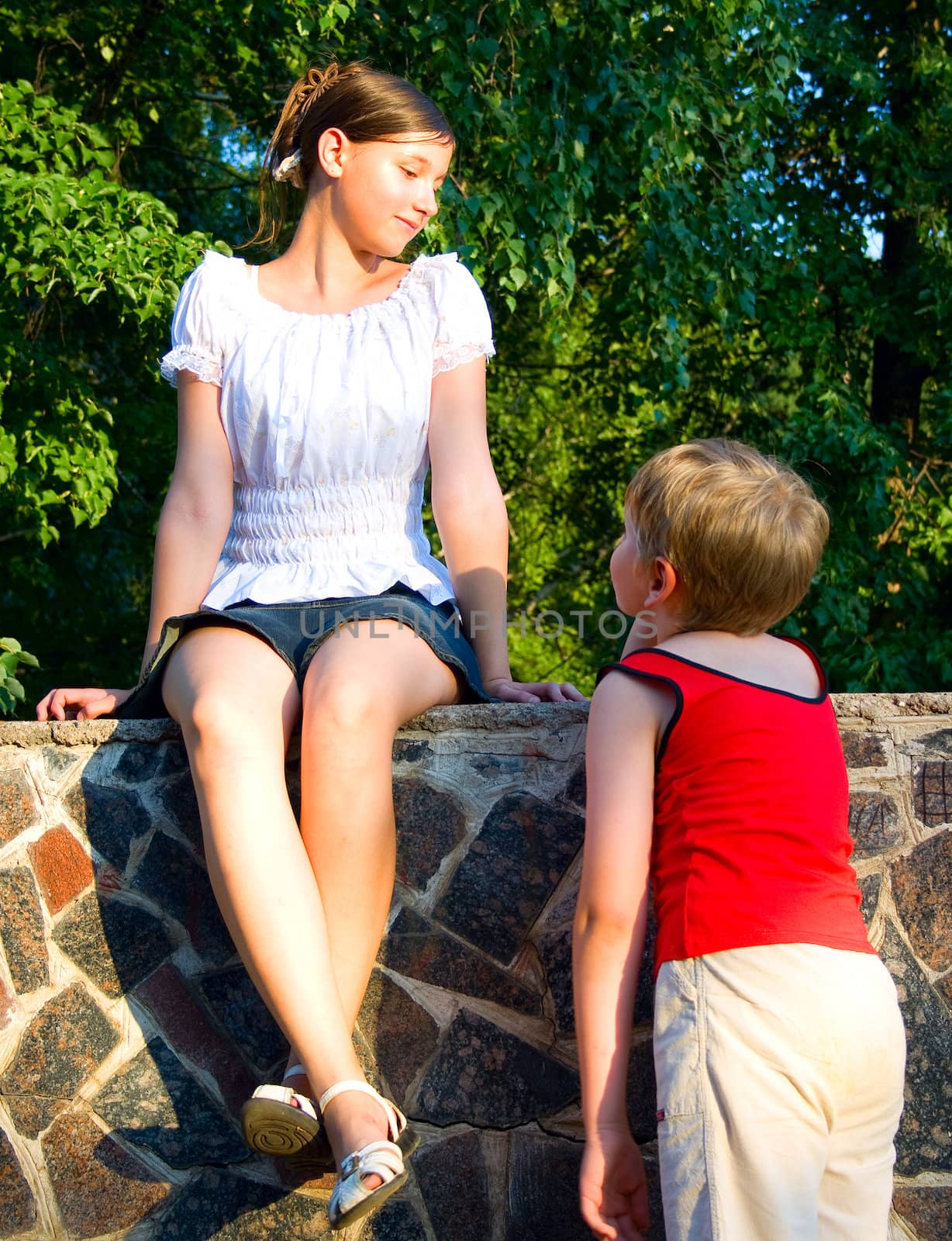 Children in park. The enamoured boy looks at the girl. The girl looks at the boy and smiles