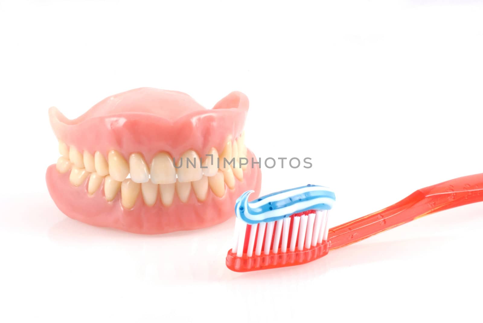 Dentures and toothbrush with toothpaste isolated on white.
